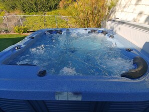 Un bain à remous à l’extérieur bleu, entouré d’un jardin où poussent différentes plantes et délimité par une clôture.