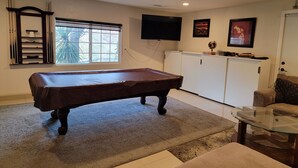 Une table de billard dans une pièce avec une fenêtre, un téléviseur, un meuble et un canapé.