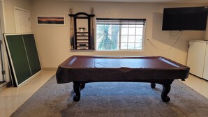 Une table de billard dans une pièce avec une fenêtre, un téléviseur et un meuble.