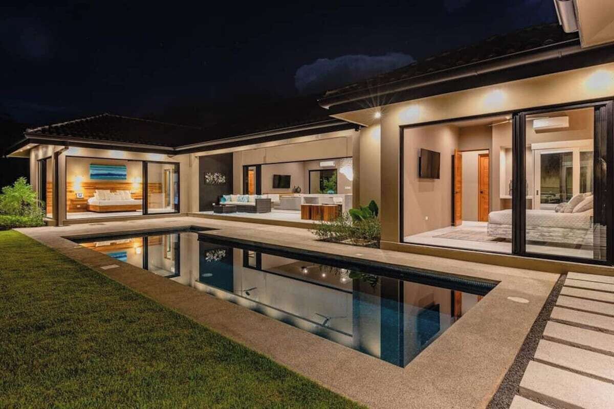A modern house with a swimming pool, large windows, and a well-lit interior.