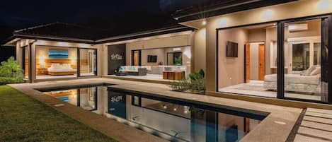 A modern house with a swimming pool, large windows, and a well-lit interior.