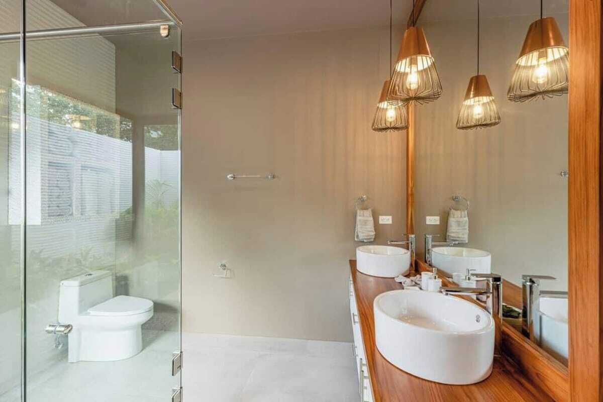 A modern bathroom with a glass shower enclosure, a white toilet, and a wooden vanity with two sinks and a large mirror.