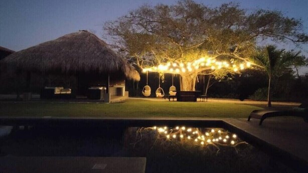A thatched-roof structure, a tree with hanging lights, and a pool with string lights.