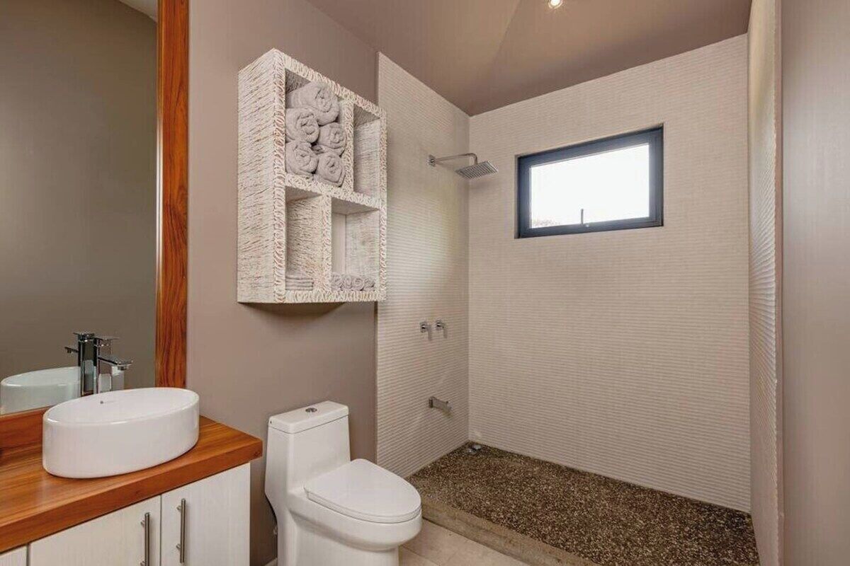 A bathroom with a wooden vanity, a white sink, a toilet, and a shower area with a window.