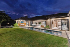 A modern house with a swimming pool, large windows, and a well-maintained lawn.