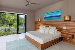A modern bedroom with a large bed, wooden headboard, and a view of greenery outside.