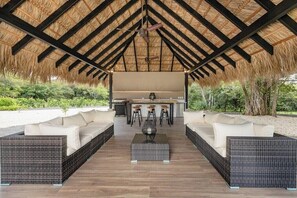 An outdoor seating area with a thatched roof, wicker furniture, and a central bar area.