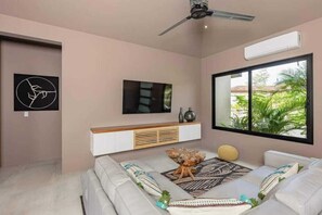 Una sala de estar moderna con un sofá, una mesa de centro, un televisor montado en la pared y un ventanal con vistas a zonas verdes.