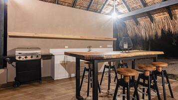 Un área de cocina al aire libre con estufa a gas, pileta y taburetes de bar.