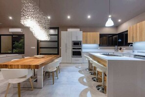 A modern kitchen with a wooden dining table, white chairs, and a central island with bar stools.