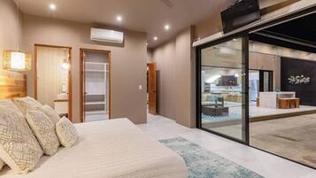 Un dormitorio moderno con cama, mesitas de noche y vista a un área de piscina a través de puertas de vidrio.