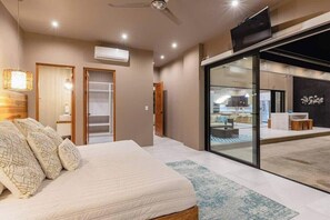 A modern bedroom with a bed, bedside tables, and a view of a pool area through glass doors.