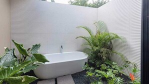 A modern bathroom with a freestanding bathtub, surrounded by lush greenery and a textured wall.