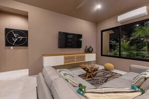 A modern bedroom with a bed, a flat-screen TV, a window with a view of greenery, and a wall-mounted air conditioner.