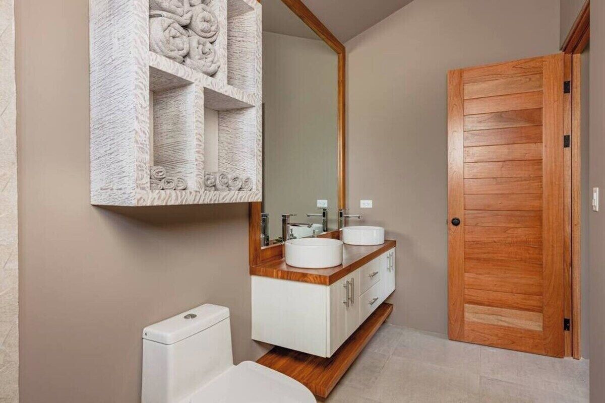 Ein Badezimmer mit einem Holzkosmetikschrank, zwei Waschbecken, einer Toilette und einem großen Spiegel.