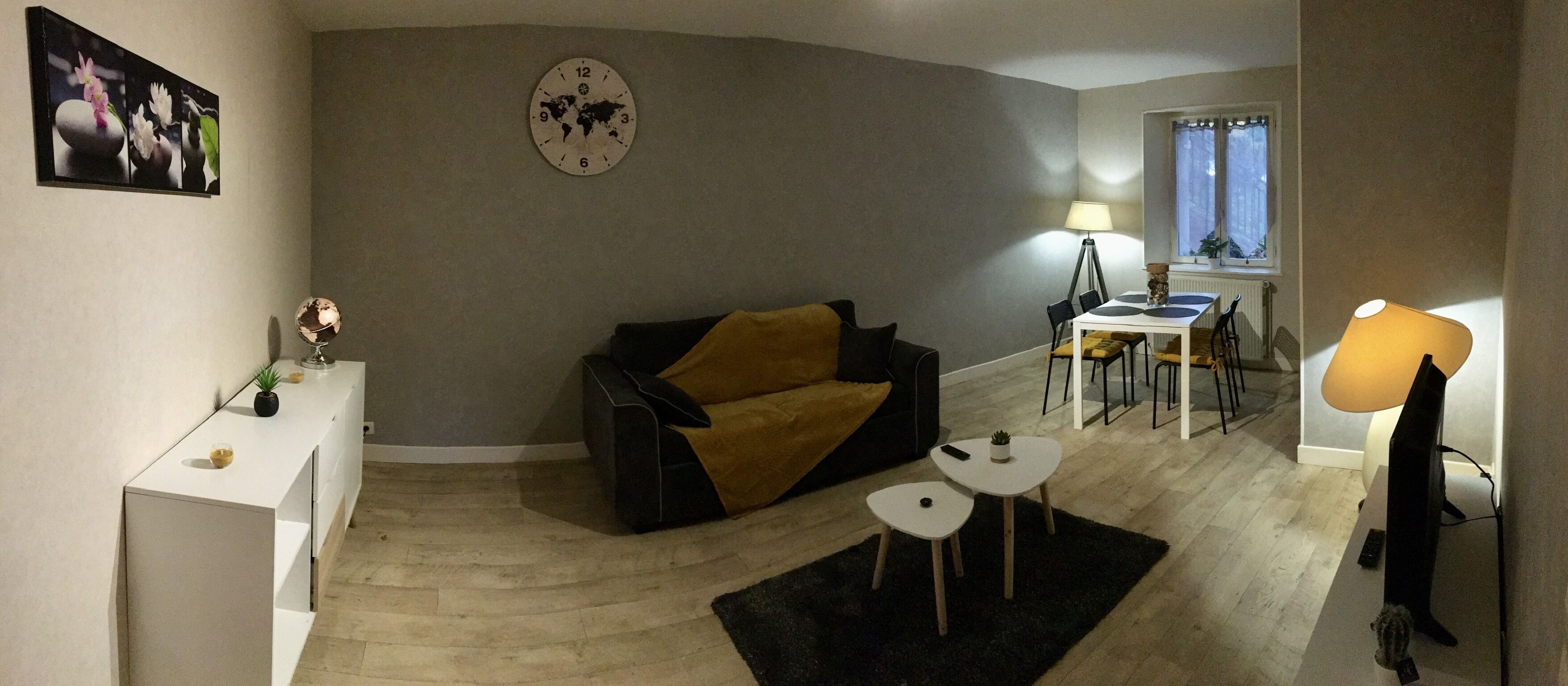 A living room with a sofa, a small table, a lamp, and a dining area with chairs.