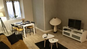 Una sala de estar moderna con un sofá, una mesa de comedor con sillas, un mueble para la televisión y una lámpara.