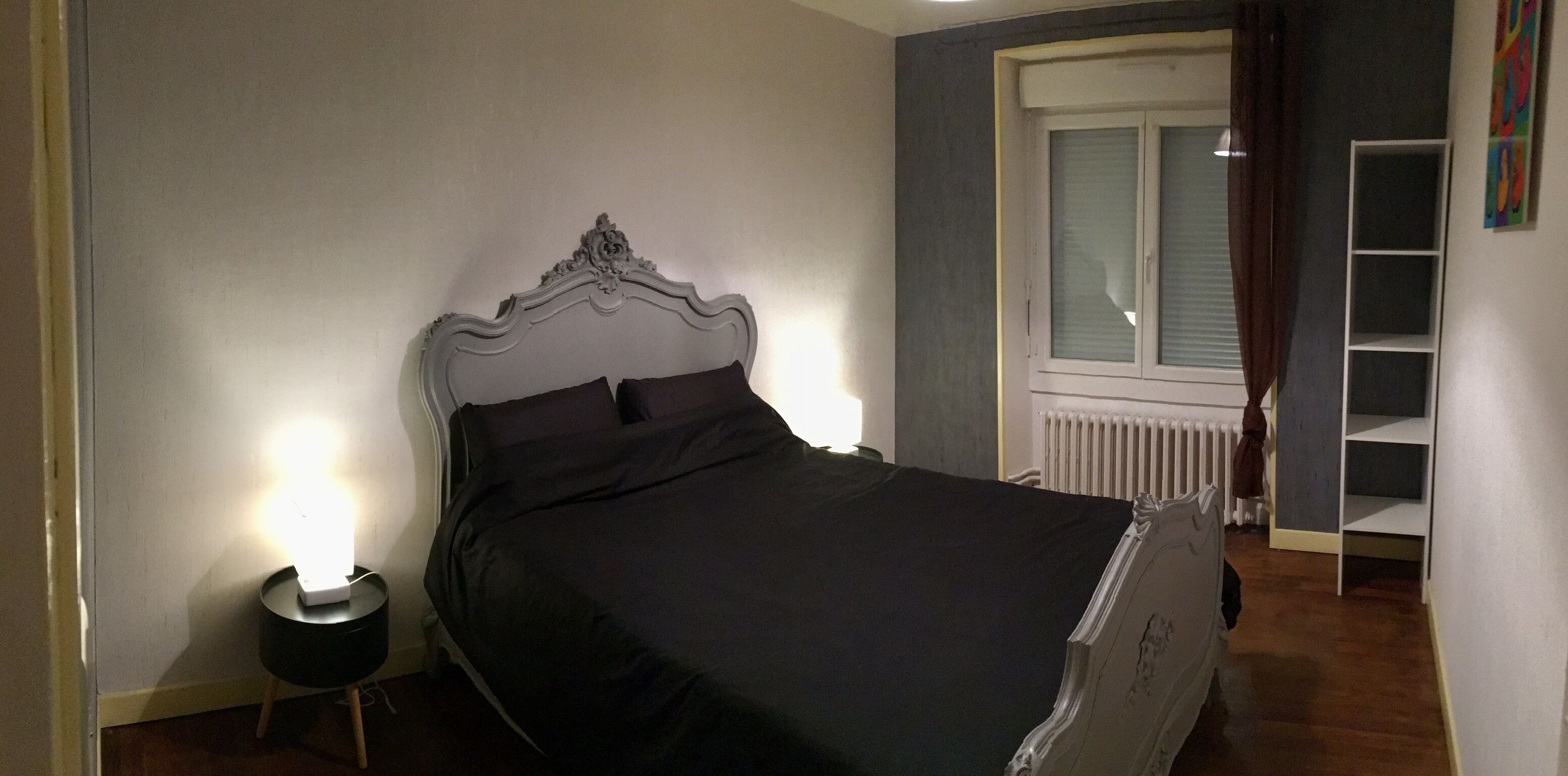 A bedroom with a bed, bedside lamp, and a window with curtains.