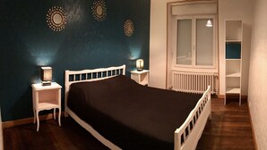 Un dormitorio con cama, dos mesitas de noche, un radiador y una ventana con persianas.