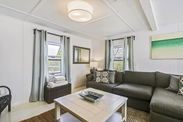 A modern living room with a sofa, a coffee table, and a window with curtains.