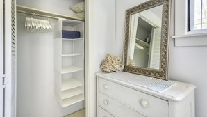 Un armario blanco con las puertas abiertas, un aparador con espejo y una ventana con persianas.