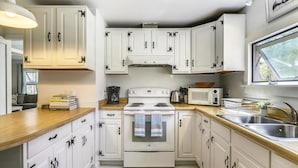 Cocina compacta con alacenas blancas, estufa, microondas y pileta.