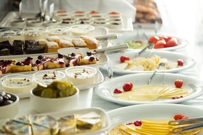 A buffet with various dishes including desserts, fruits, and salads.