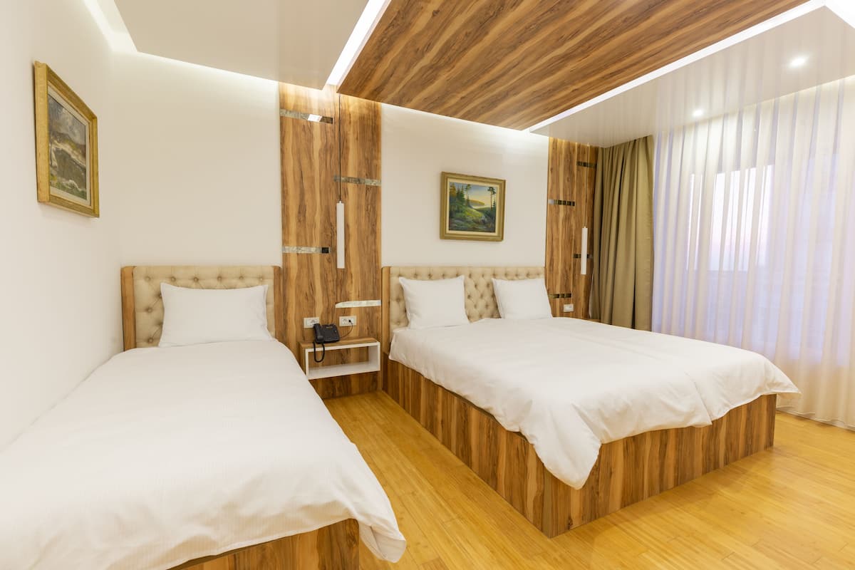 Een hotelkamer met twee bedden, houten wandbekleding, een schilderij en een raam met gordijnen.