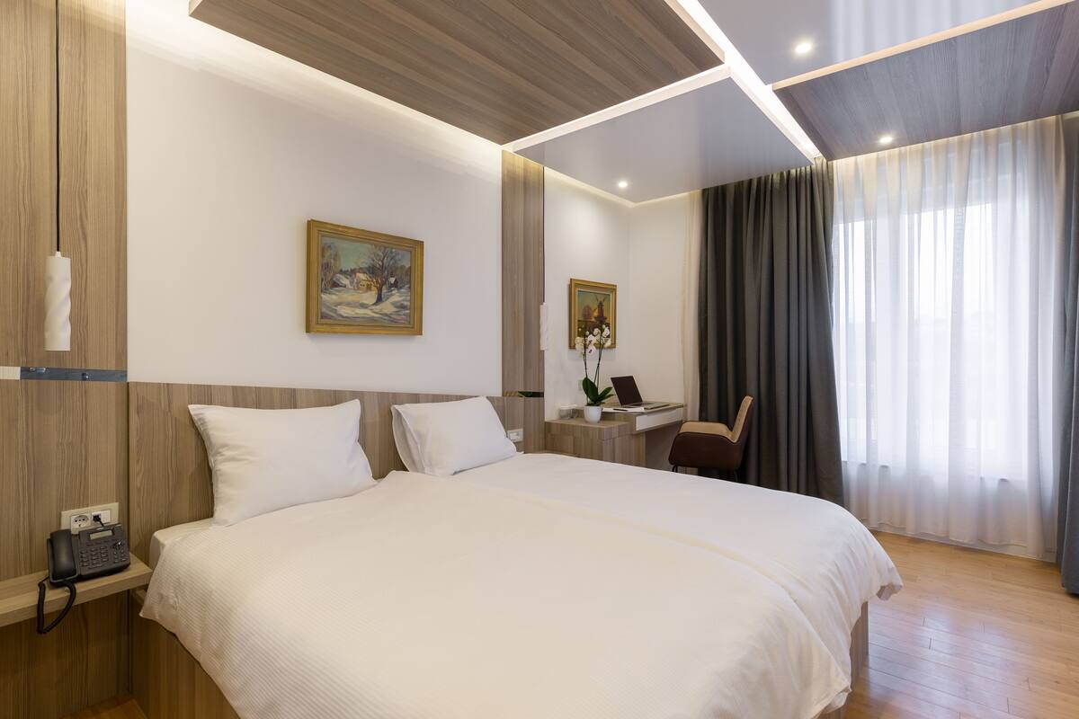 Een moderne hotelkamer met een groot bed, een bureau met een laptop, een telefoon en een schilderij aan de muur.