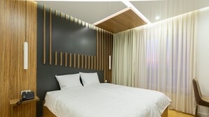 A modern hotel room with a large bed, wooden paneling, a telephone on a nightstand, and a chair. - Star Hill Hotel & SPA (Pristina)
