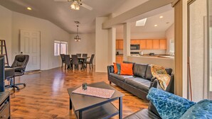 Ein geräumiges Wohnzimmer mit dunklem Holzboden, einem schwarzen Ledersofa mit orange- und blauen Kissen, einem Couchtisch mit einem gemusterten Untersetzer und einem Deckenventilator.