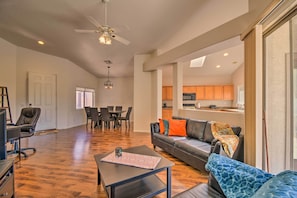 A spacious living room with a dark wooden floor, a black leather sofa with orange and blue cushions, a coffee table with a patterned placemat, and a ceiling fan. - Gated Golf community, 3 Bedrooms-2 Bath, Central location, w/ views of South MTN (Phoenix)