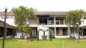 A two-story building with a balcony, surrounded by palm trees and a well-maintained lawn. - Vivens Bed & Breakfast Sarchi (Sarchí Sur)