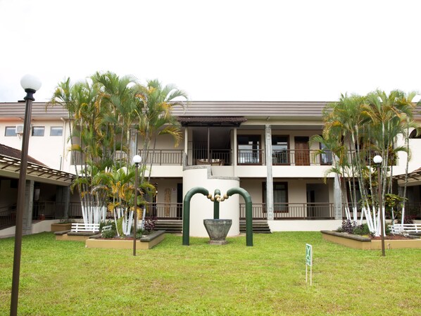 A two-story building with a balcony, surrounded by palm trees and a well-maintained lawn.