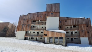 Un edificio de varios pisos con fachada de madera, balcones y una pista de esquí al fondo.