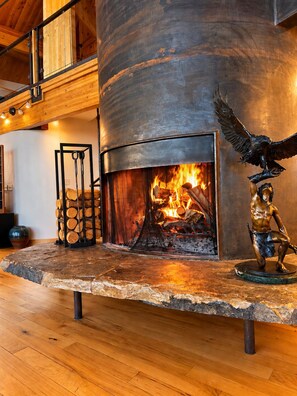 A modern interior with a central fireplace, a wooden ceiling, and a metal sculpture.
