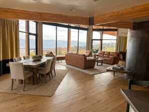 A spacious living area with a wooden dining table, sofas, and a large window offering a mountain view.