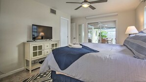 A bedroom with a bed, a television on a cabinet, a ceiling fan, and a view of an outdoor patio. - Single open-concept home one block from the ocean with heated pool and lanai  (West Palm Beach)