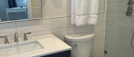 A bathroom with a white sink, dark cabinets, a toilet, and a shower area.