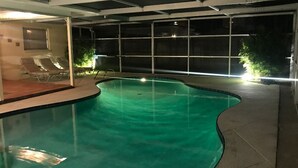 An indoor swimming pool with a curved design, surrounded by lounge chairs and a covered area with a view of the night sky. - Single open-concept home one block from the ocean with heated pool and lanai  (West Palm Beach)