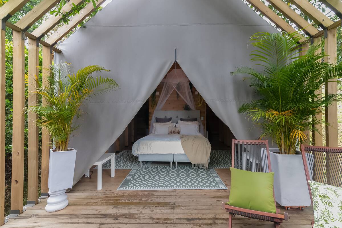 A tented accommodation with a bed, a small table, and two chairs.