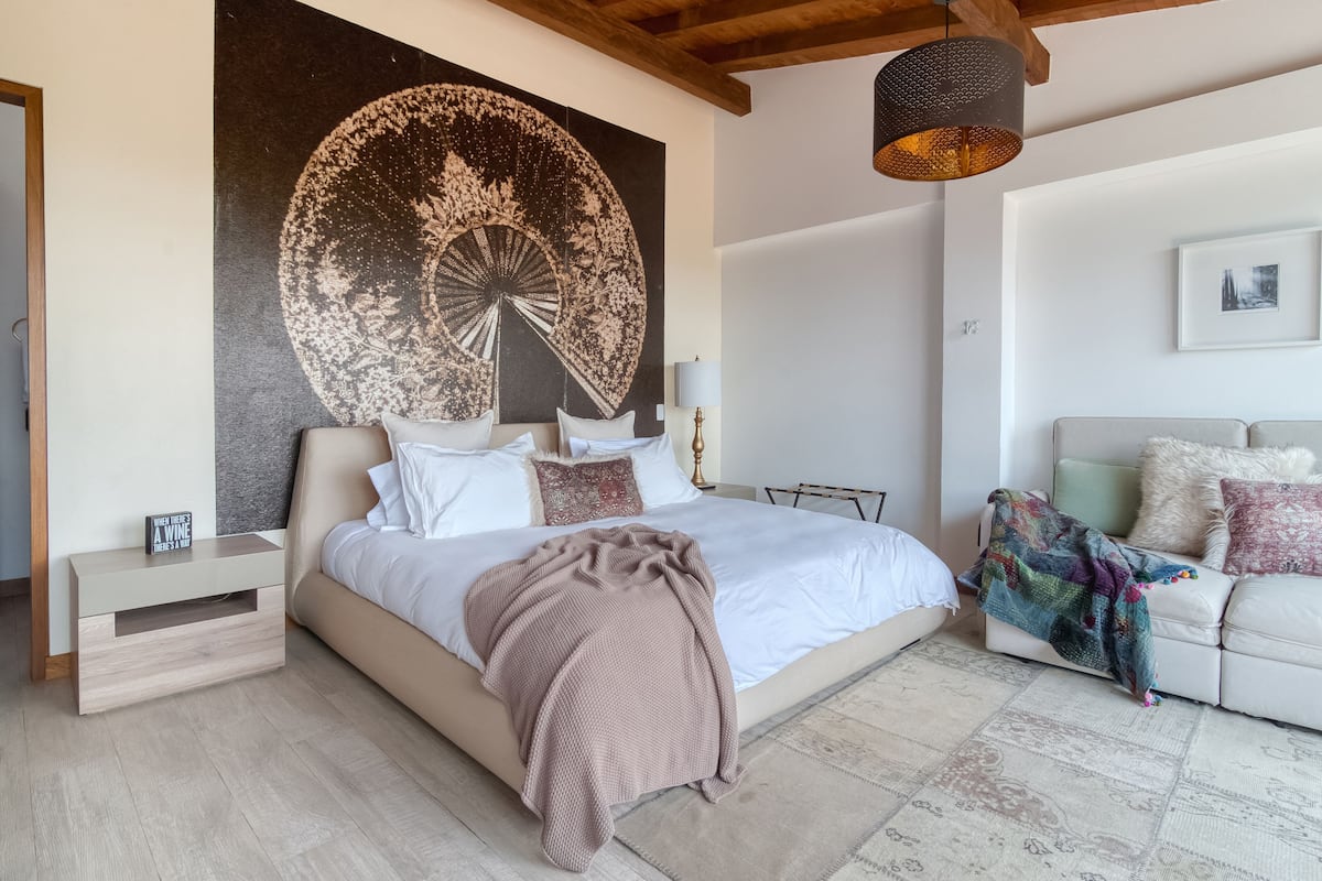 A bedroom with a large bed, a nightstand, a sofa, and a wall art piece.
