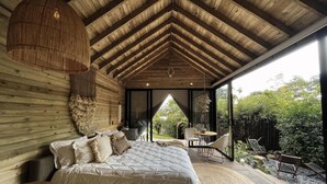 Een ruime slaapkamer met een groot bed, een hanglamp en uitzicht op het landschap door een glazen deur.