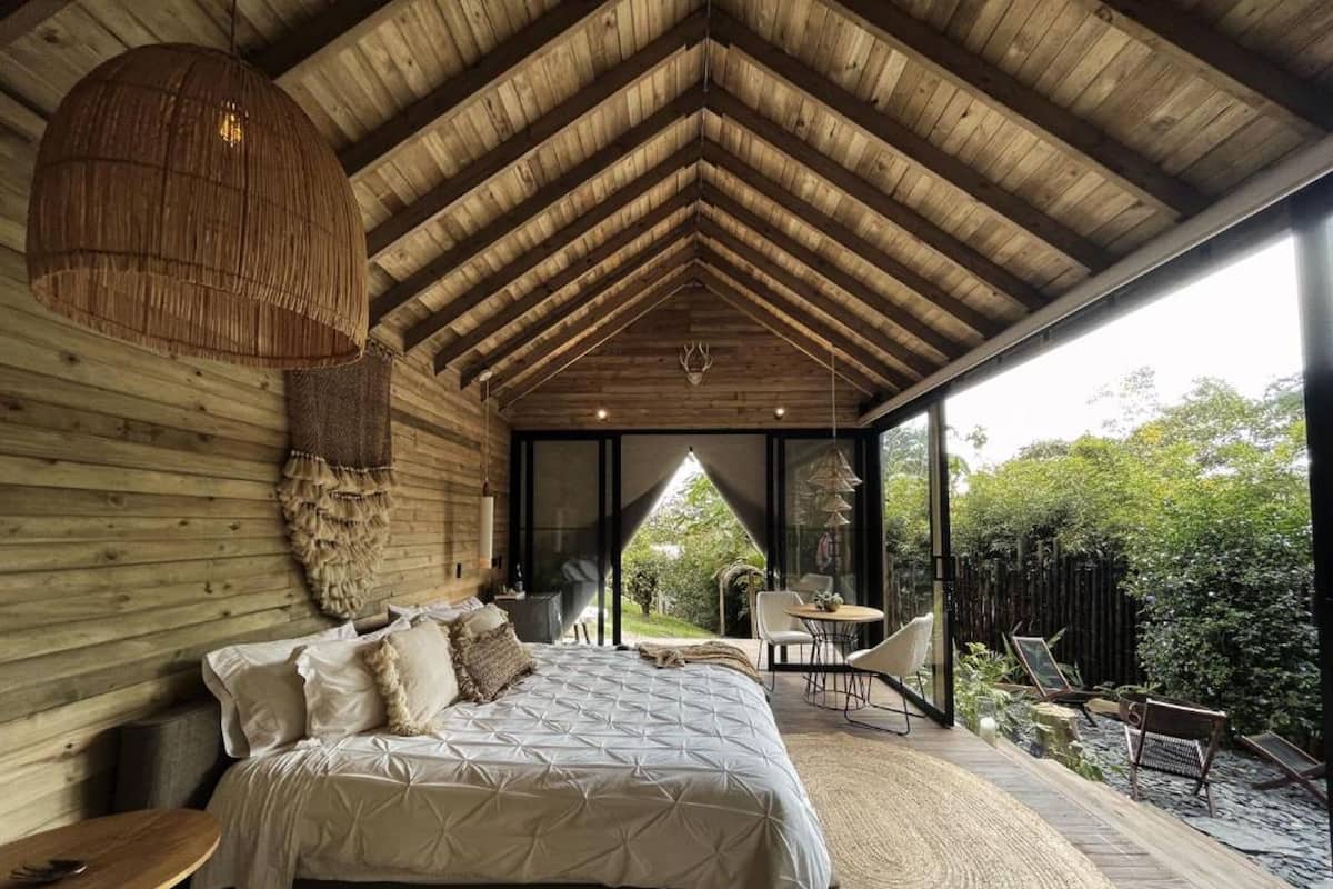 A spacious bedroom with a large bed, a hanging light fixture, and a view of the outdoors through a glass door.