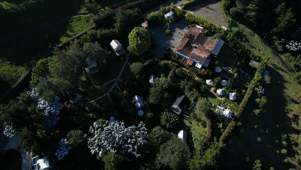 Luchtbeeld van een woonwijk met een huis met pannendak, omringd door weelderige begroeiing en een verzorgde tuin met witte bloeiende planten.