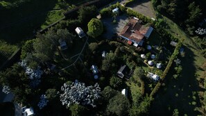 Vista aérea de uma área residencial com uma casa de telhado telhado, cercada por vegetação exuberante e um jardim bem cuidado com plantas brancas floridas.