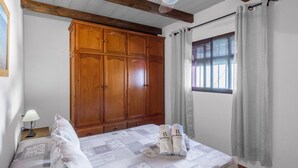 Une chambre à coucher avec une grande armoire en bois, un lit recouvert d’une couvre-lit à motifs et une fenêtre avec des rideaux.