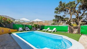 Une piscine rectangulaire à l’eau d’un bleu limpide, entourée d’une clôture verte et agrémentée d’un portail en bois. Plusieurs chaises longues blanches sont disposées le long du bord de la piscine.
