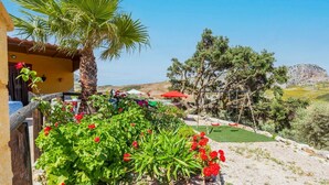 Un jardin avec un palmier, des fleurs rouges et une balançoire.
