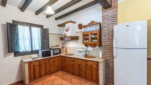 Een keuken met houten kastjes, een witte koelkast, een magnetron en een spoelbak.